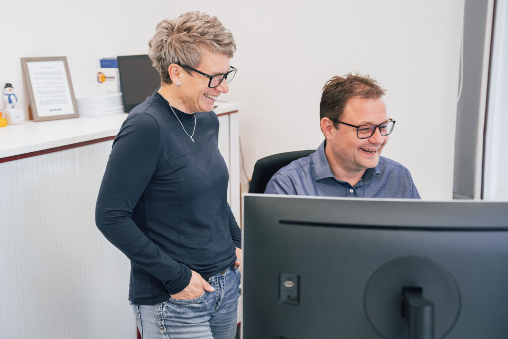 Zwei Mitarbeitende der Ahrens Steuerberatungsgesellschaft mbH in Hermannsburg lachen gemeinsam vor dem Bildschirm – kollegialer Austausch und Teamarbeit in der Steuerberatung